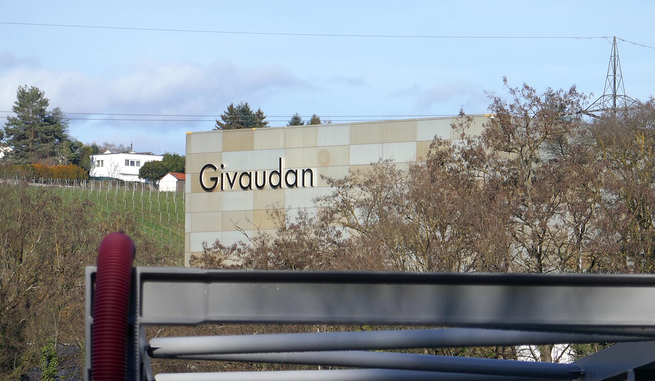 Bâtiment de Givaudan avec enseigne en grandes lettres, vu depuis la passerelle de Chèvres.